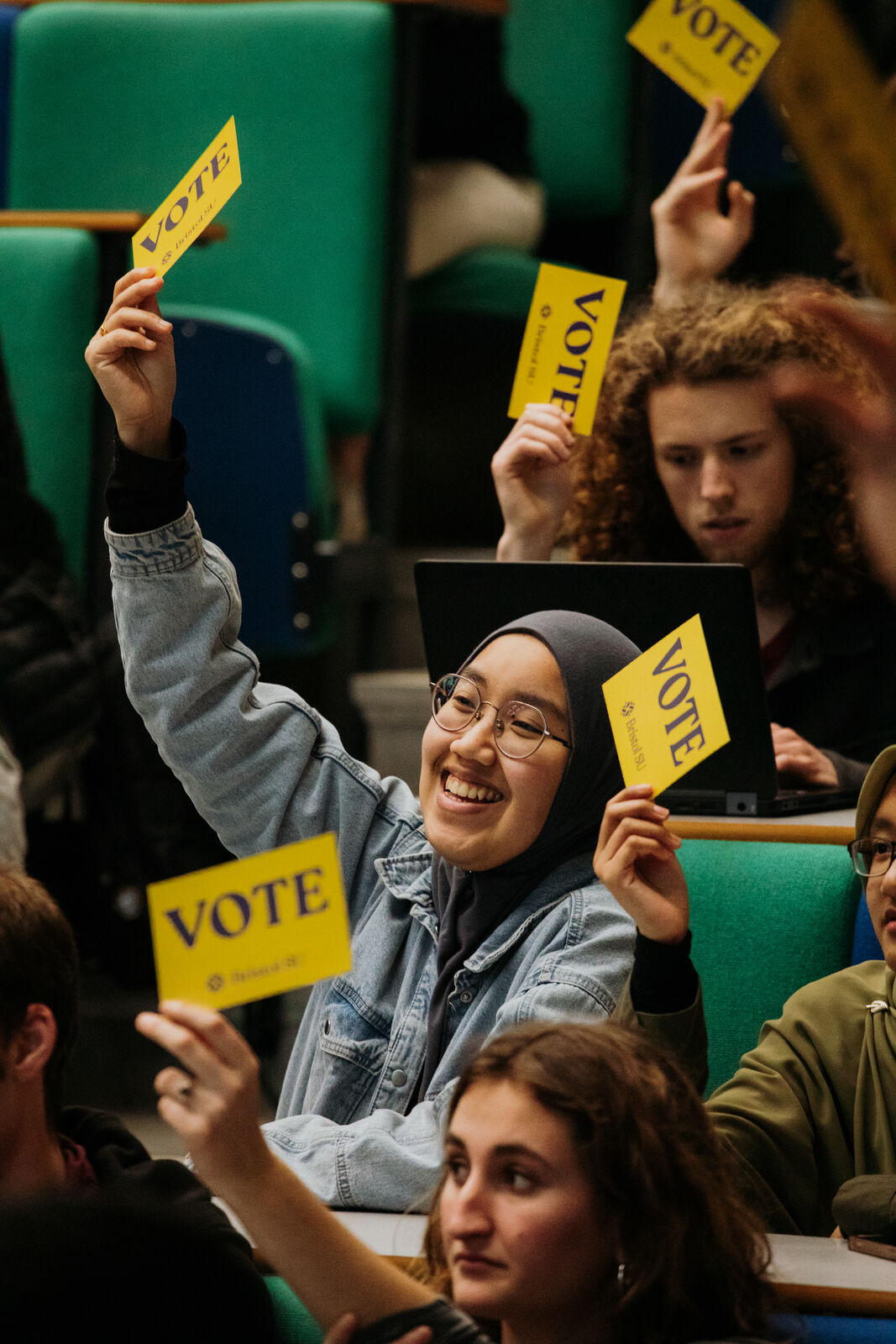 Students hold up yellow cards with the word VOTE on.